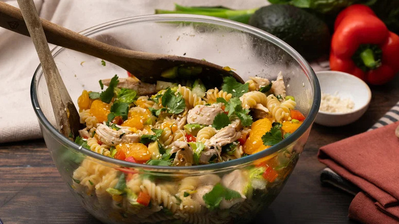 Mandarin Chicken Pasta Salad in large glass bowl with wooden utensils