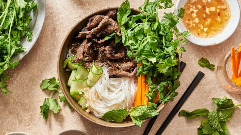 Steak and Vermicelli Noodle Bowl with Nuoc Cham in brown bowl surrounded by accoutrements