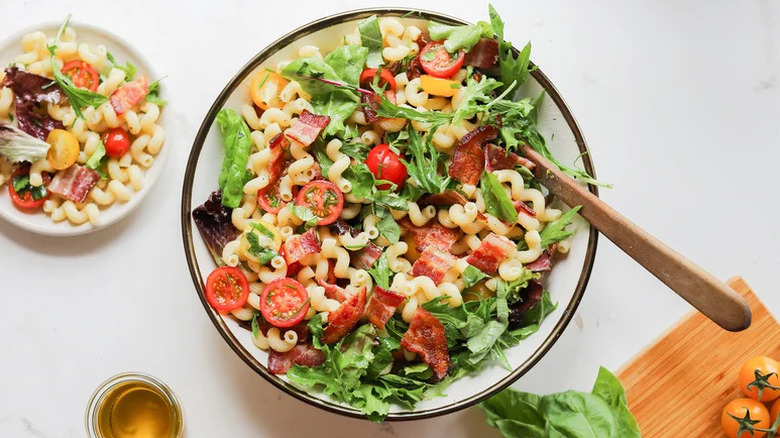 Summer BLT Pasta Salad in white and black bowl with wooden spoon