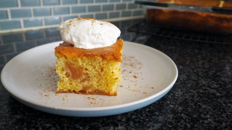 Slice of apple cake on plate, topped with dollop of cool whip