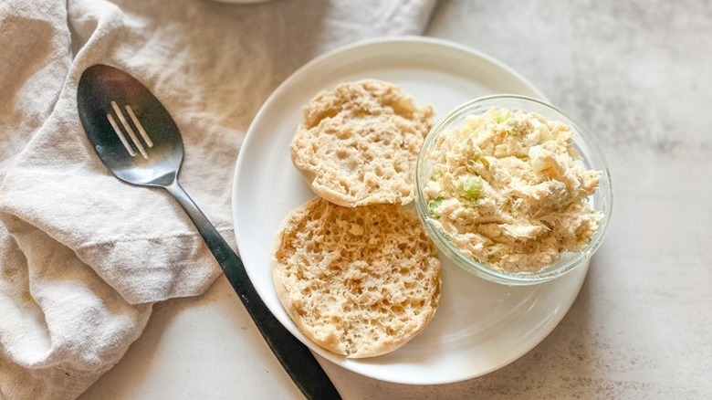 Bowl of chicken salad on a plate with a sliced bread roll