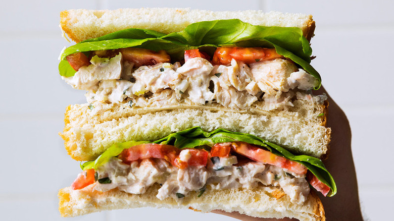 Hand holding a stack of chicken salad sandwiches with lettuce and tomato