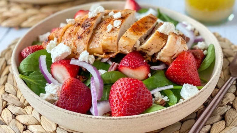 Bowl of grilled chicken and strawberry salad with sliced red onion and crumbled feta