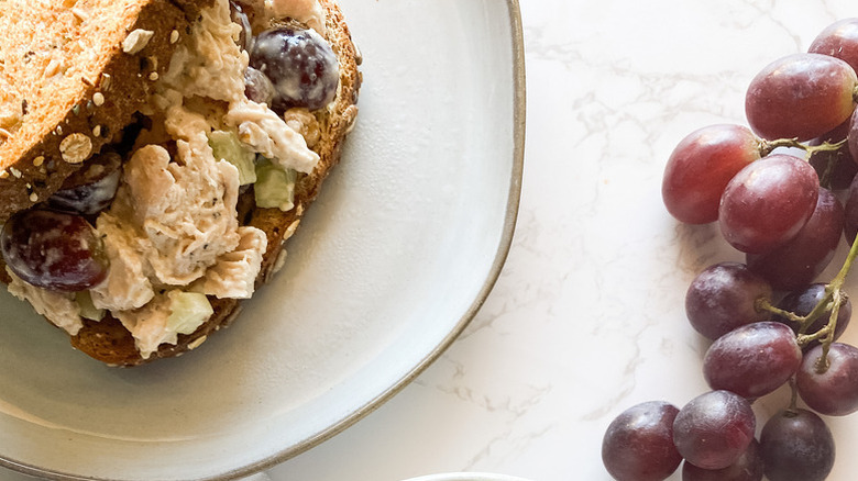 Chicken salad sandwich on a plate next to a bunch of red grapes