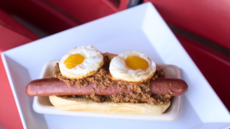 Hot dog with taco meat and two fried eggs on red plate