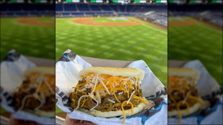 Meat and cheese-filled arepa on paper with blurred field in background
