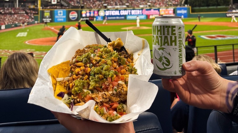 Hands holding nachos and beer can in front of blurred field
