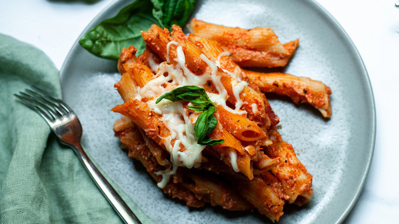 Portion of baked ziti with melted cheese on plate, garnished with basil
