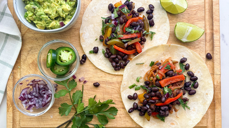 Black bean tacos on wooden board with selection of toppings