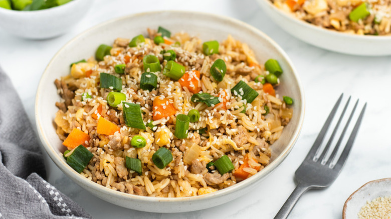 Bowl of pork and vegetable fried rice garnished with sesame seeds and chopped green onions
