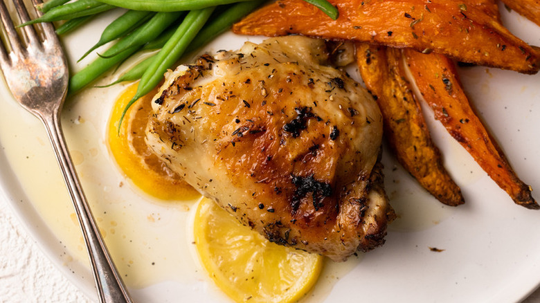 Baked chicken thigh on plate with lemon rounds, green beans, and sweet potato wedges