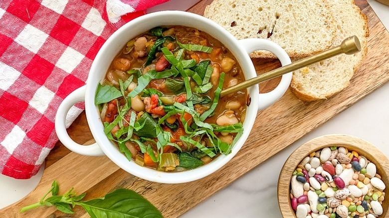 Bowl of bean soup garnished with basil, on wooden serving board with slices of bread