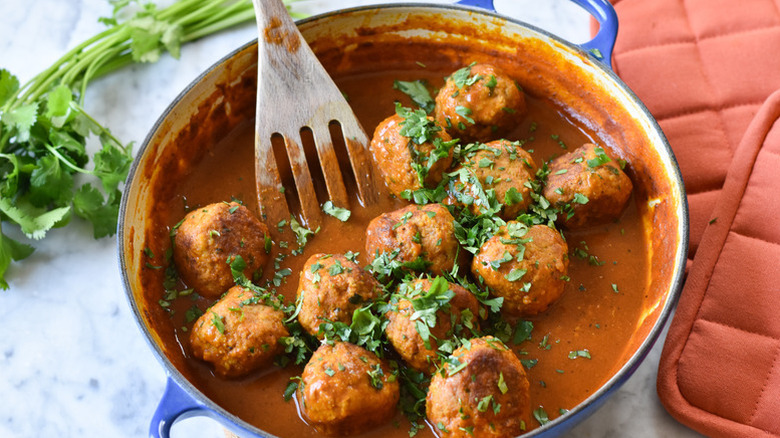 Turkey meatballs in casserole pot with tomato sauce and fresh herb garnish