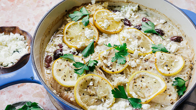 Baked fish in casserole pot with lemon slices, crumbled feta, and fresh parsley