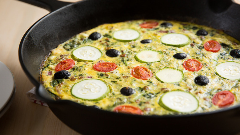 Lentil frittata in skillet, topped with zucchini slices, cherry tomatoes, and black olives