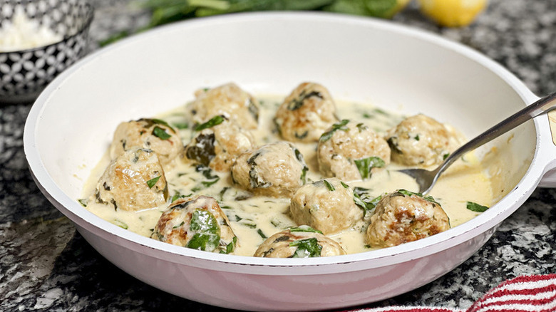 Chicken, spinach, and feta meatballs in white bowl with creamy sauce