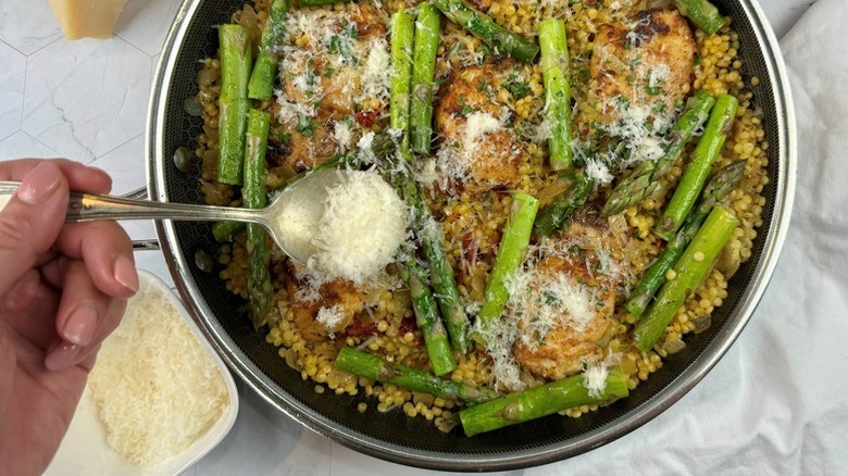 Sprinkling Parmesan cheese over pot of chicken and asparagus couscous