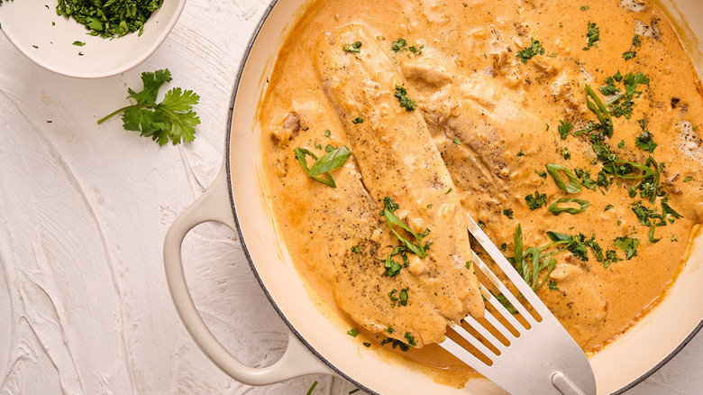 Tilapia in casserole pot with creamy sauce and fresh herb garnish