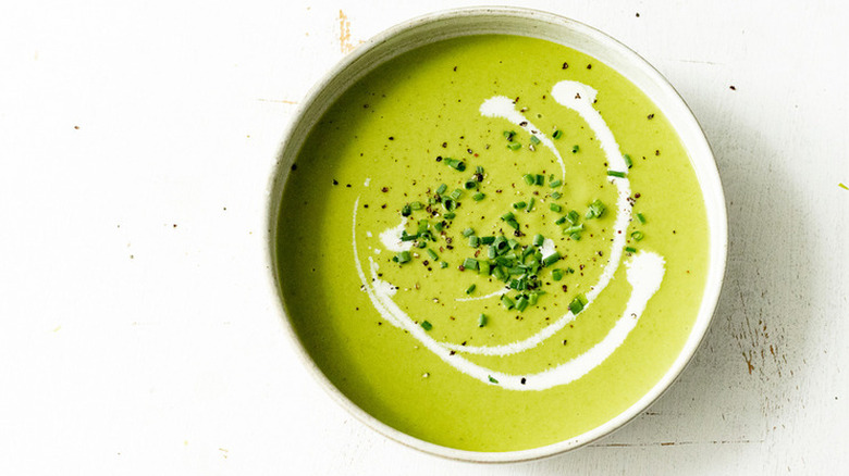Top view of a bowl of asparagus soup garnished with cream and chopped chives