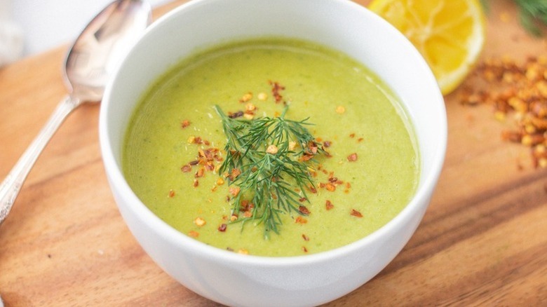Bowl of cream of asparagus soup with fresh dill and red pepper flakes served on a wooden board with lemon in the back
