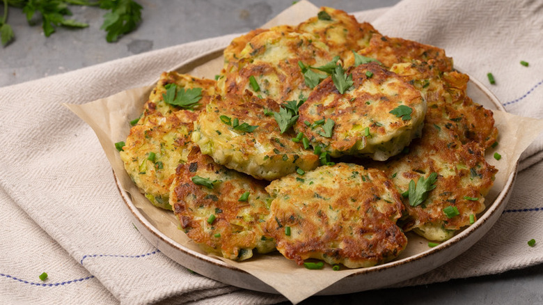 Pile of leek and cheddar fritters on plate garnished with fresh herbs an served on a kitchen towel