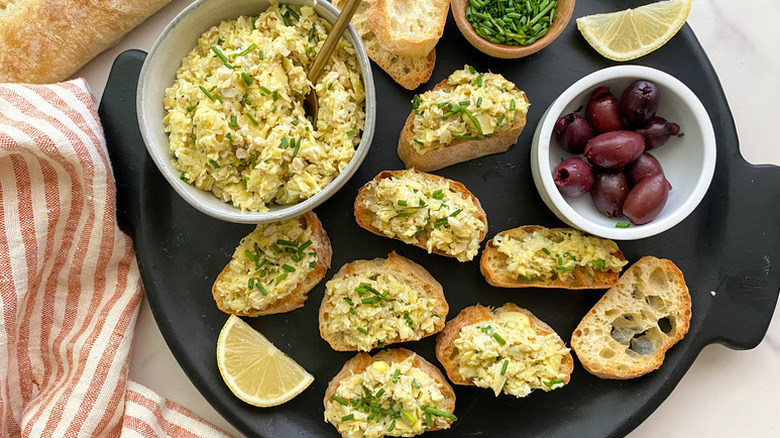 Creamy lemon-artichoke crostini on serving platter with bowl of black olives