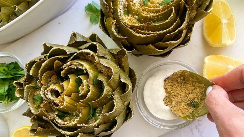 A person spoon a creamy dip with roasted Parmesan-stuffed artichokes served with a side of lemons