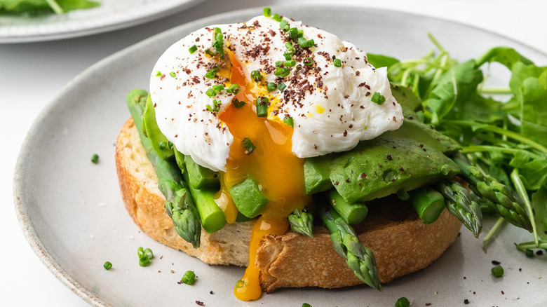 Slice of sourdough toast topped with avocado, asparagus, and poached egg