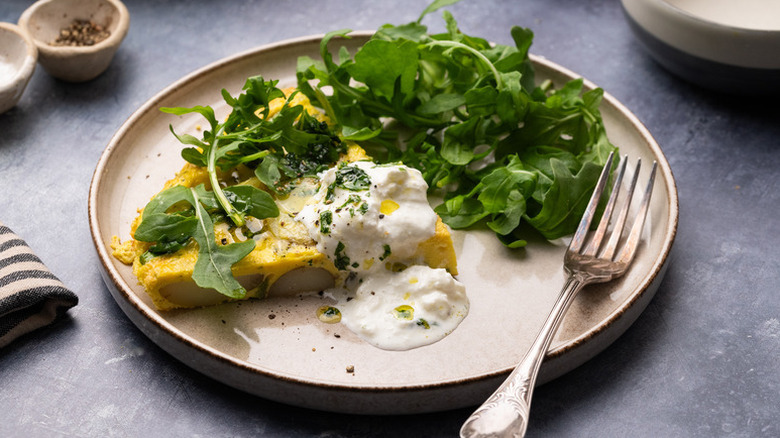 Slice of asparagus frittata on plate with melty burrata on top and arugula on the side