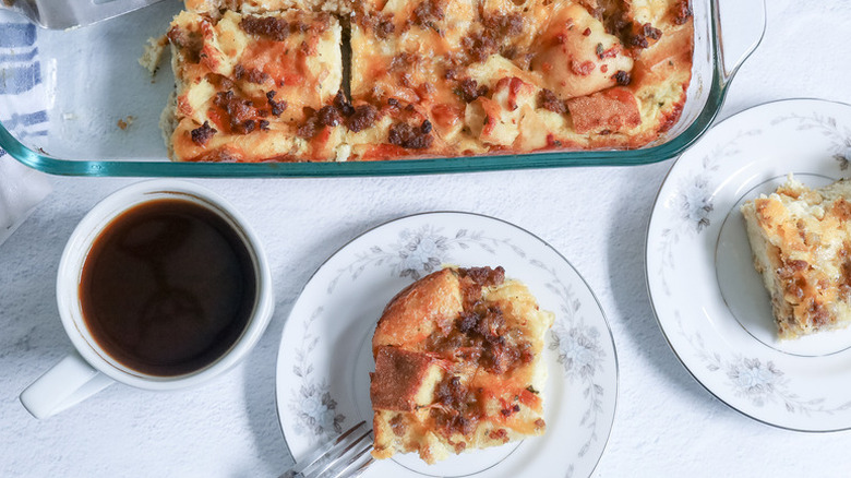 Sausage strata served from casserole dish onto plates, next to mug of coffee