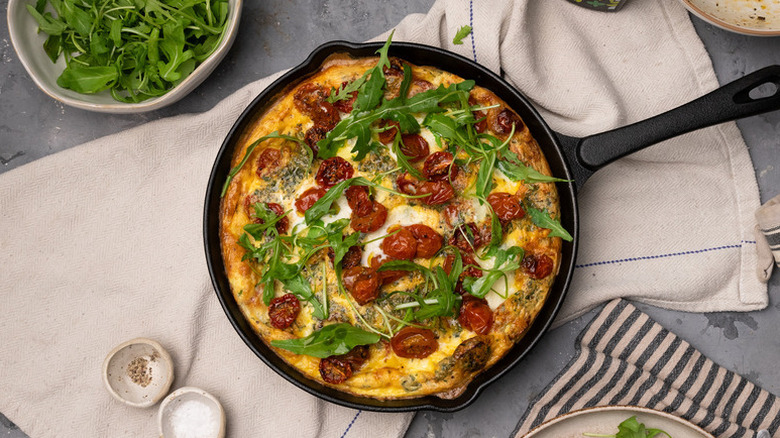 Caprese frittata in skillet, topped with arugula