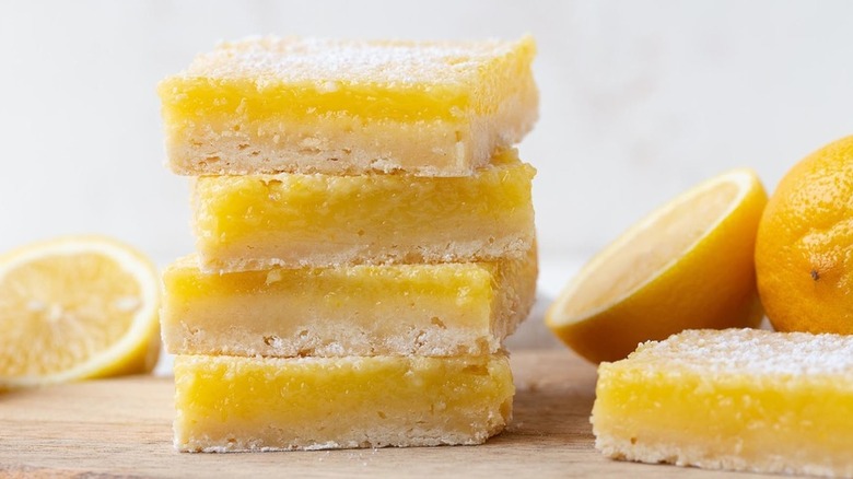 Stack of lemon bars on wooden board, next to fresh lemon halves