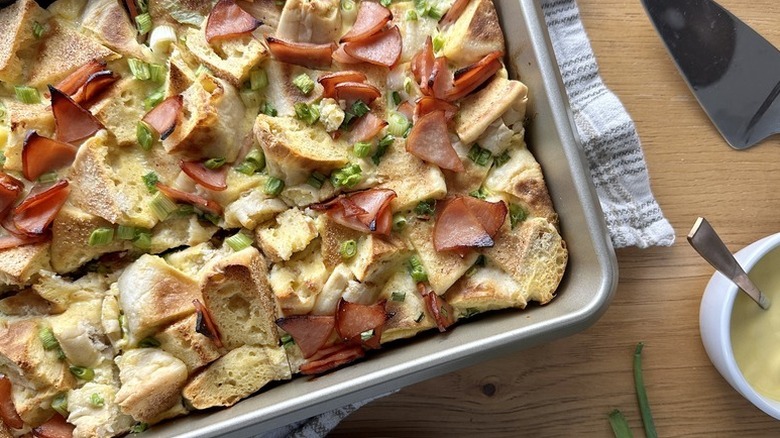 Eggs Benedict casserole in baking dish next to pot of Hollandaise sauce