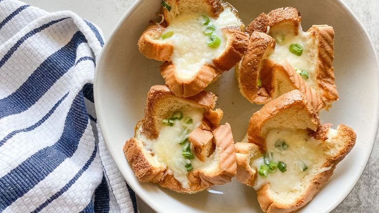 Four baked egg toast cups in white bowl