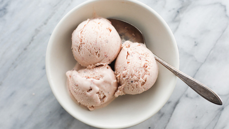 Three scoops of strawberry ice cream in bowl with spoon