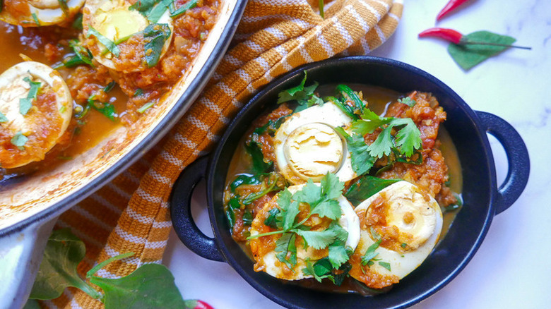 Spicy egg curry in casserole dishes, garnished with cilantro