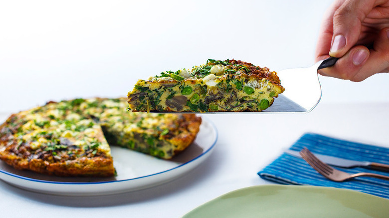Lifting slice of vegetable frittata from plate with metal slice