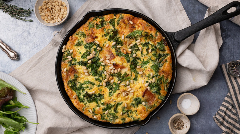 Sweet potato and kale frittata in skillet, garnished with pine nuts