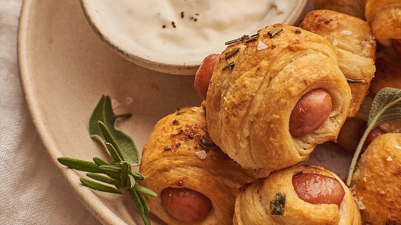 Close up of pigs in blankets on plate with bowl of creamy dip