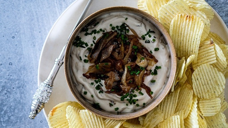 Bowl of caramelized onion dip on plate with ridged potato chips
