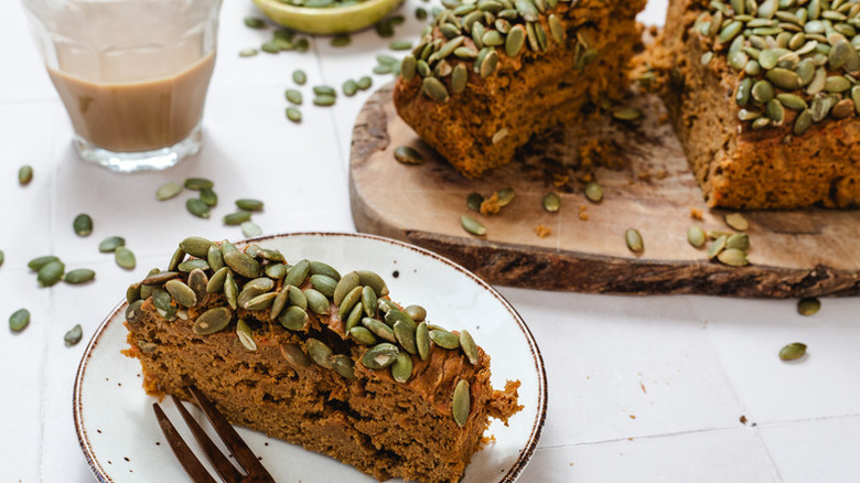 Slice of pumpkin seed-topped pumpkin bread served from wooden board onto plate