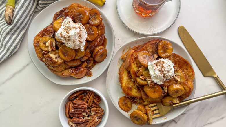 Bananas foster French toast on plates, topped with whipped cream and pecans