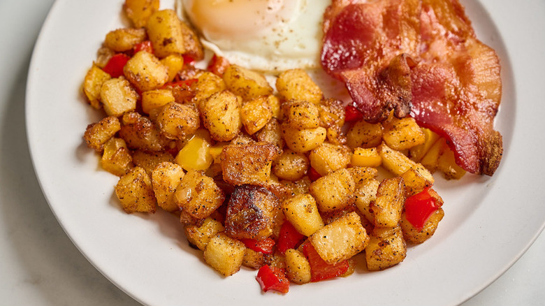 Home fries on plate with bacon and fried egg