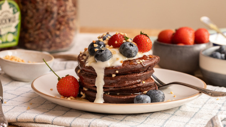 Stack of chocolate pancakes on plate, topped with yogurt and berries