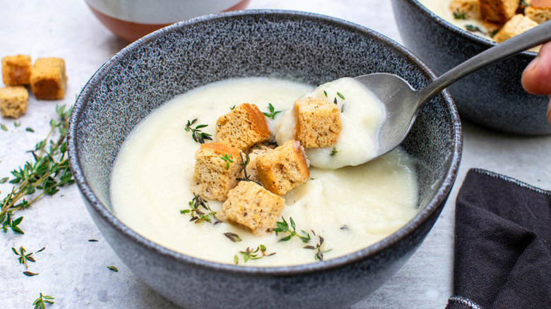 Cauliflower cheese soup in bowl with croutons and fresh thyme