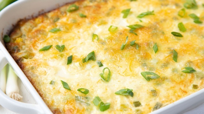 Creamy corn pudding in white baking dish, garnished with chopped green onion