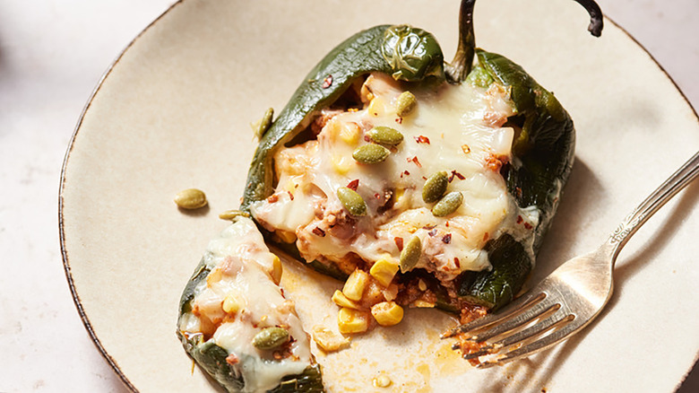 Cheesy stuffed roasted poblano pepper on plate with fork, sprinkled with pepitas