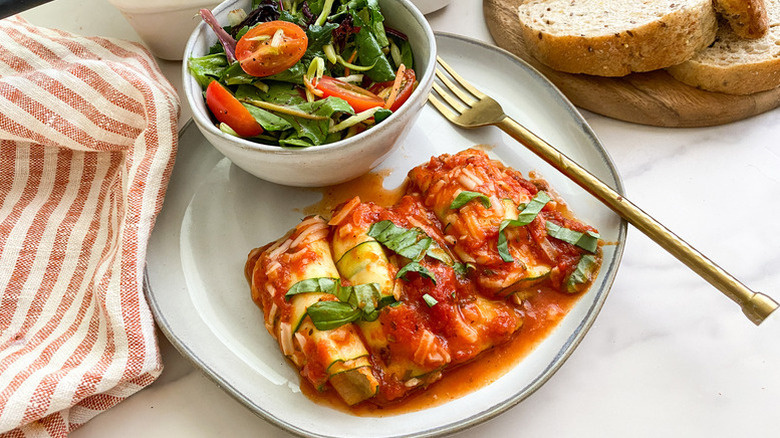Zucchini lasagna roll-ups on plate with bowl of salad