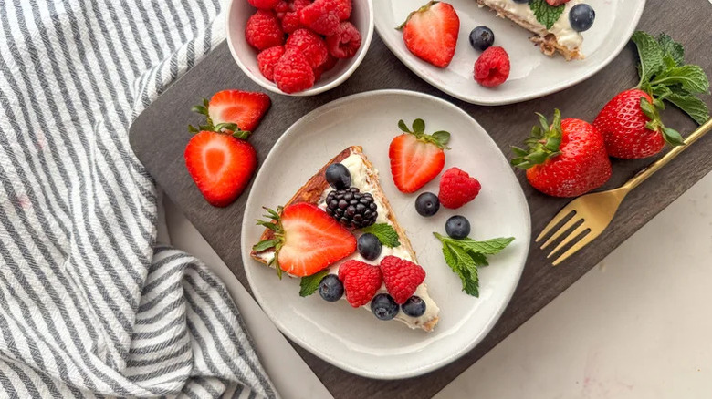 Breakfast Fruit Pizza with Cinnamon Roll Crust on white plate surrounded by fruit