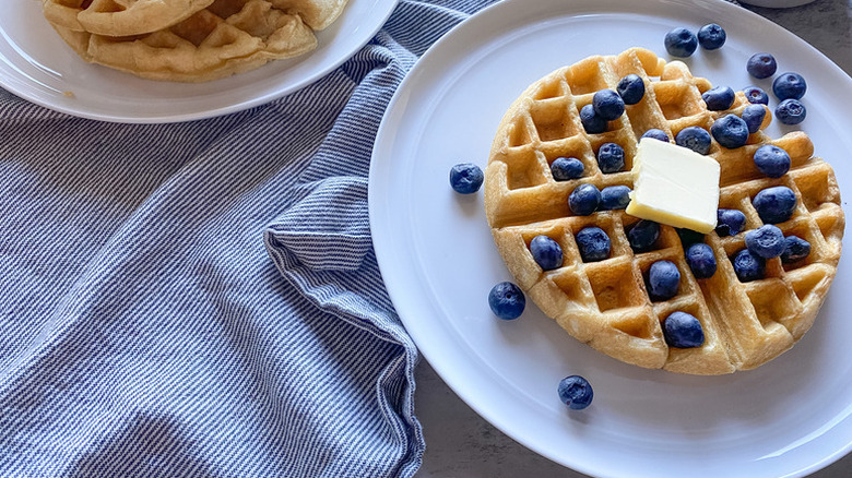 Buttermilk waffles on plate, topped with pat of butter and fresh blueberries